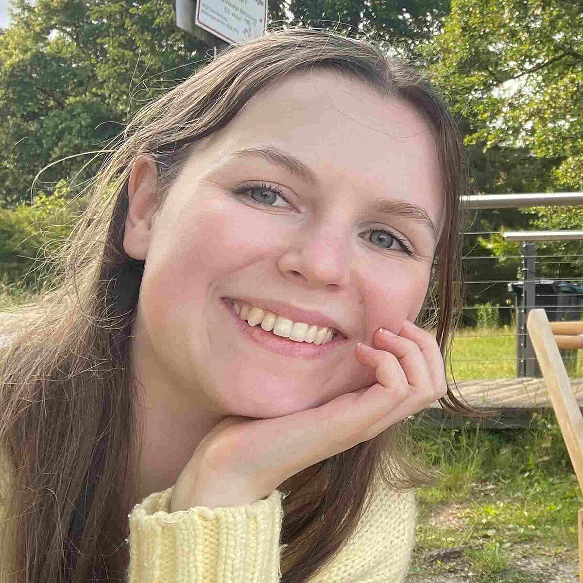 Interviewpartnerin Vanessa Hergert aus der Kindertagesstätte Striesener Entdeckerland lächelt in die Kamera, im Hintergrund ist viel Grün zu sehen