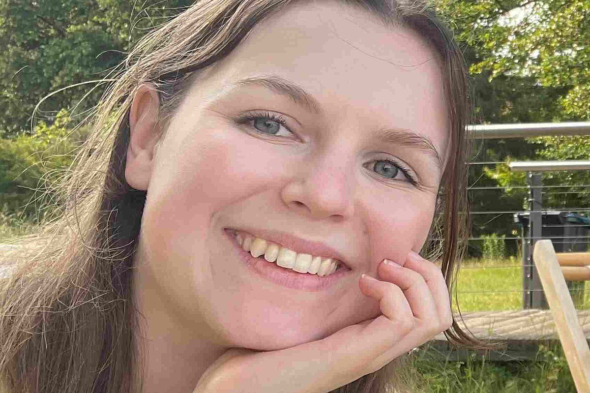 Interviewpartnerin Vanessa Hergert aus der Kindertagesstätte Striesener Entdeckerland lächelt in die Kamera, im Hintergrund ist viel Grün zu sehen