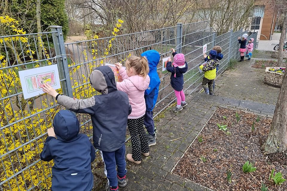 Kinder befestigen selbst gestaltete Flaggen und Bilder am Bauzaun des Kindergartens, um internationale Vielfalt darzustellen.