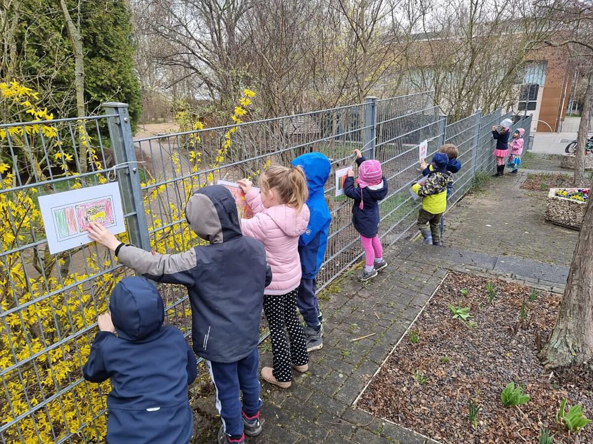 Kinder befestigen selbst gestaltete Flaggen und Bilder am Bauzaun des Kindergartens, um internationale Vielfalt darzustellen.