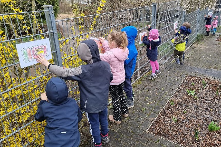 Kinder befestigen selbst gestaltete Flaggen und Bilder am Bauzaun des Kindergartens, um internationale Vielfalt darzustellen.