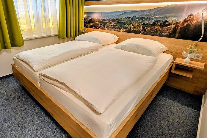 Akademiehotel Jena – Doppelzimmer 2025 Modern eingerichtetes Doppelzimmer im Akademiehotel mit großem Bett, Holzrahmen, Wandbild mit Landschaftspanorama und Fenster mit grünen Vorhängen