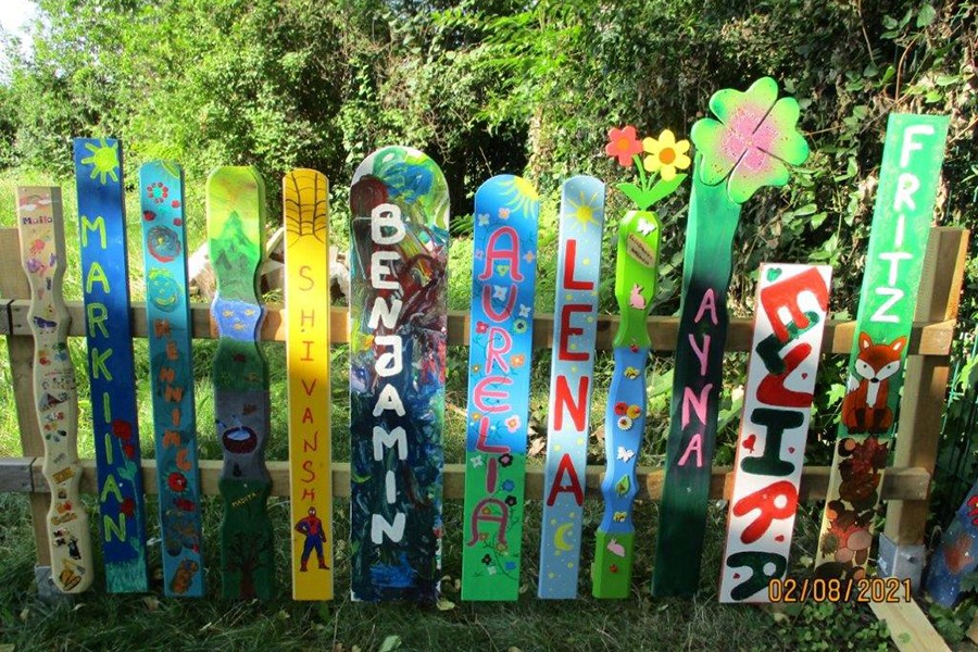Zu sehen sind bunte Zaunslatten, die von Kindern gestaltet wurden. Sie sind an dem Zaun angebracht, der unseren Forschergarten eingrenzt.