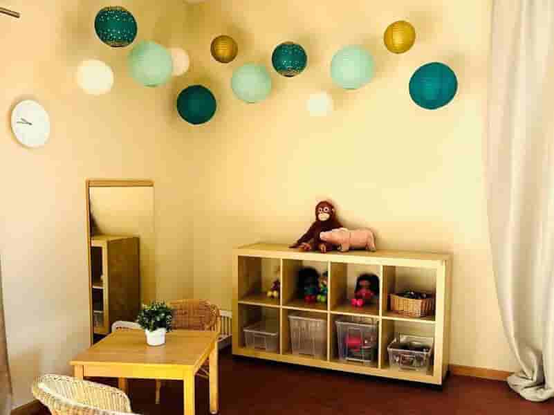 Puppenecke im Kindergarten – Rollenspielbereich mit Spielmöbeln und Kuschelecke Gemütliche Puppenecke im Kindergarten mit Kindertisch, Spielmöbeln, Regal mit Spielsachen und dekorativen Wandgirlanden