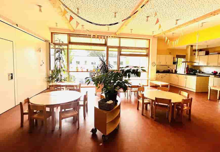 Kinderrestaurant im Kindergarten – Gemeinsames Essen in heller Wohlfühlatmosphäre Helles Kinderrestaurant im Kindergarten mit kleinen Holztischen und Stühlen, Pflanzen, großer Fensterfront und freundlicher Essensatmosphäre