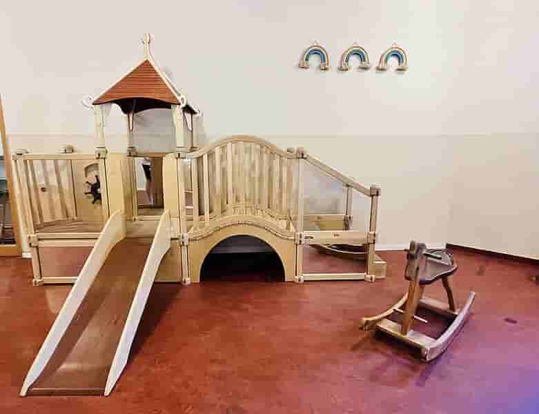 Bewegungslandschaft im Kindergarten – Kletterspielplatz mit Rutsche und Balanciergeräten Holz-Kletterspielplatz im Kindergarten mit Rutsche, Podest, Tunnel, Balanciersteg und Schaukeltier auf rotem Boden