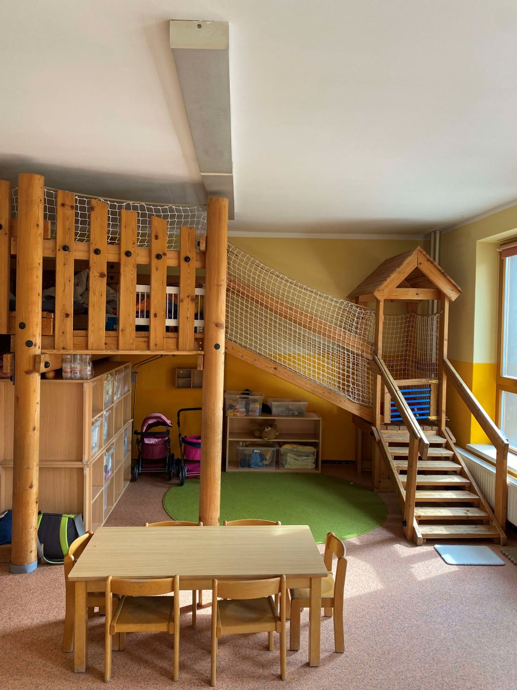 Raum im Kindergarten Vollbrachtfinken mit Holzpodest, Kletterrampe und Tischgruppe für gemeinsames Spielen und Basteln.