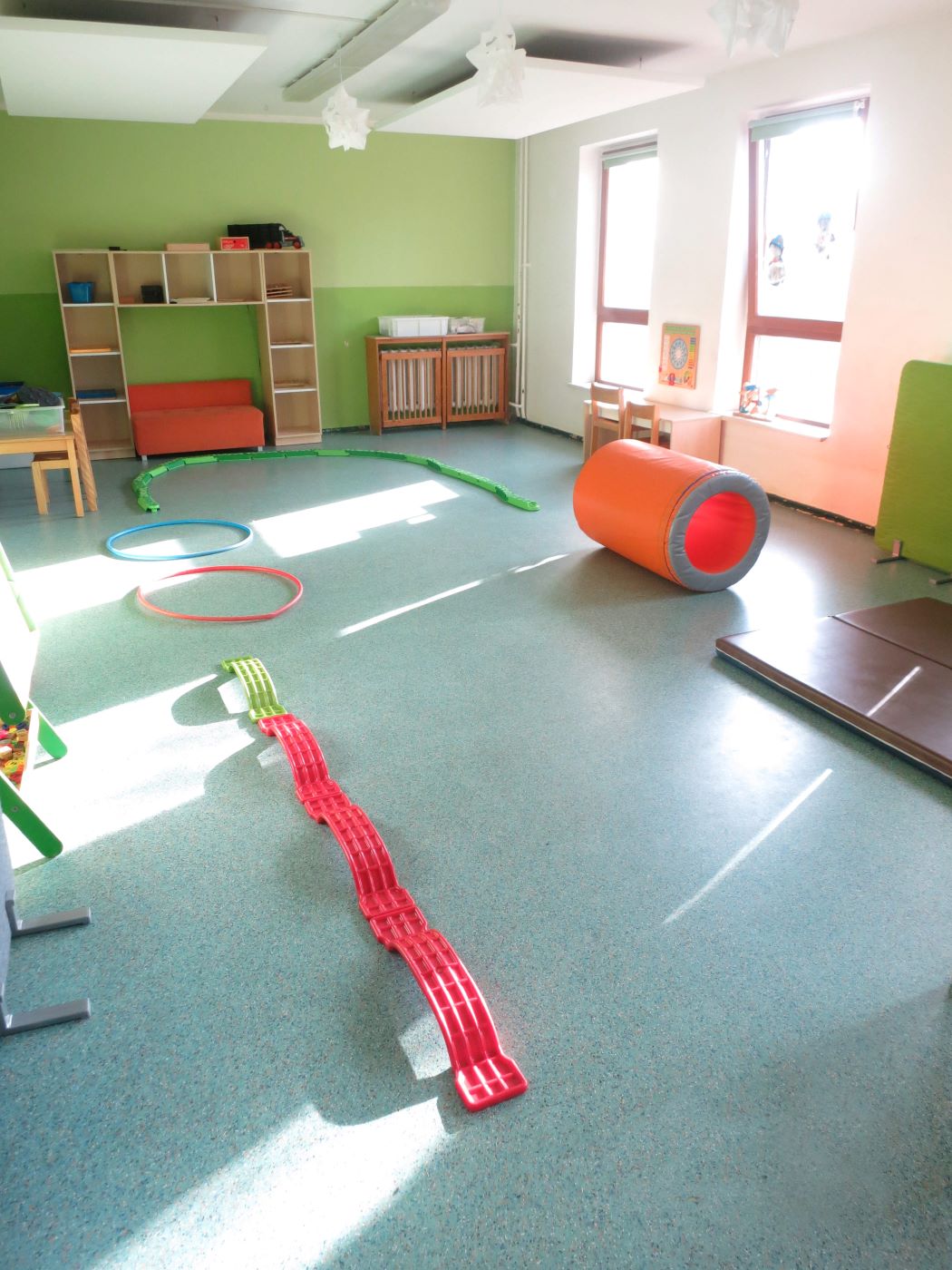 Bewegungsraum mit bunten Sportgeräten wie Reifen, Matten und Kletterelementen für motorische Förderung.
