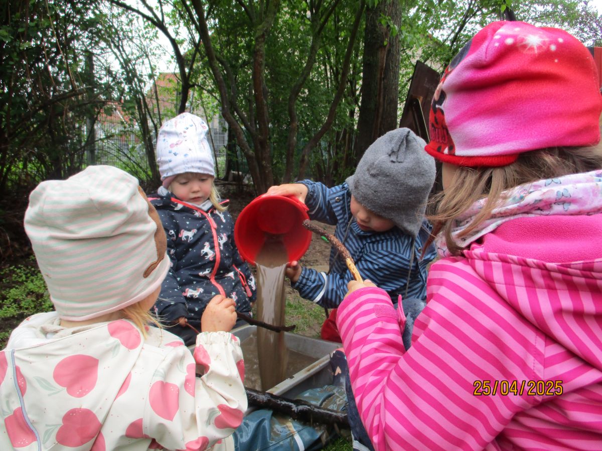 Ein Kind schüttet einen Eimer aus, in dem er zuvor Wasser mit Erde und Sand gemischt hat