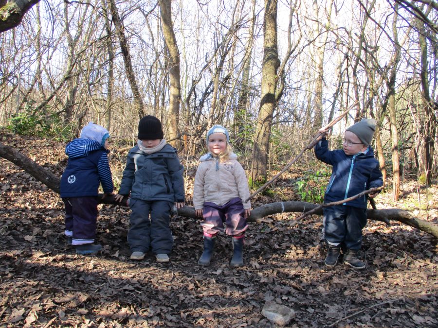 Die Kinder sitzen auf einem querliegenden Holzstamm im Wald und spielen